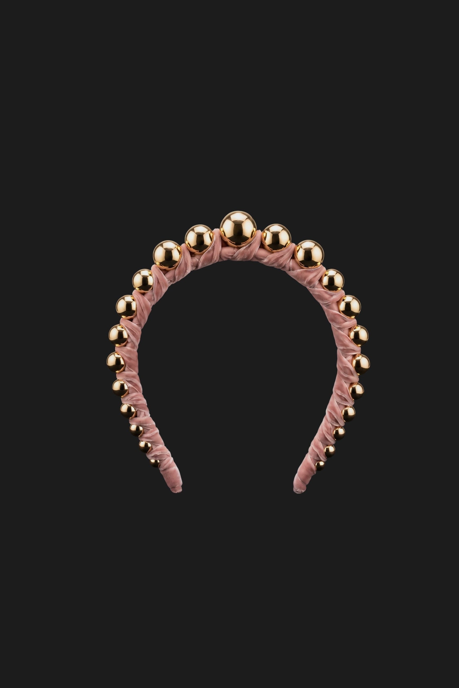 A dusty pink velvet headband adorned with a row of shiny gold metallic beads, shown against a solid black background.