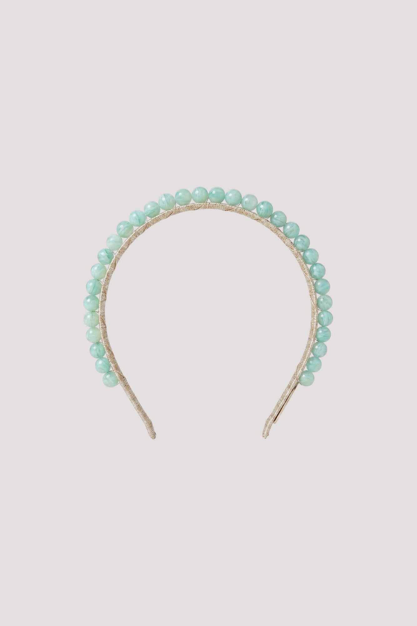A delicate headband featuring a row of small, light mint green beads set in a thin gold-tone metal band, shown against a solid light gray background.