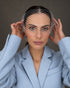 A woman wearing a light blue blazer and a silver birdcage veil, adjusting the veil for spring racing trends photoshoot 2026