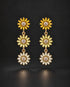 A pair of gold dangle earrings featuring three stacked sunburst flower motifs with clear gemstones, set against a dark black background.